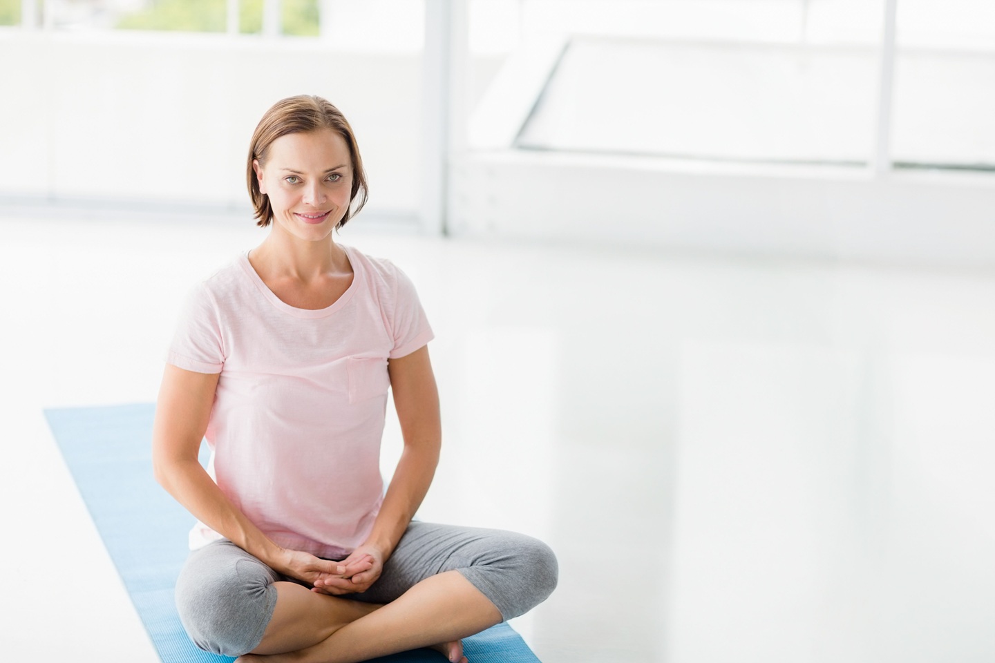 woman is sitting cross legged on blue yoga mat